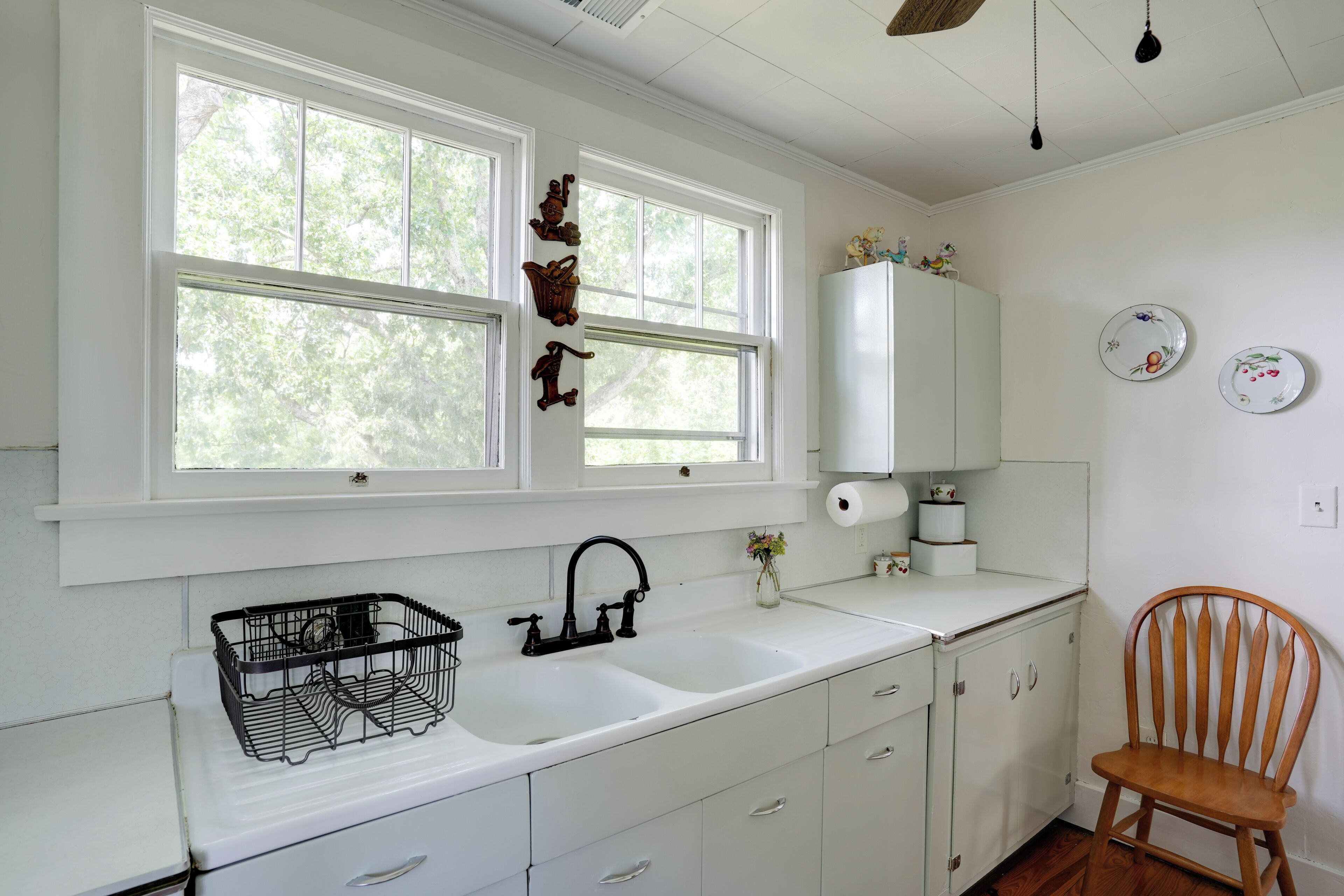 Una cocina con armarios blancos, un lavamanos doble y una silla de madera.
