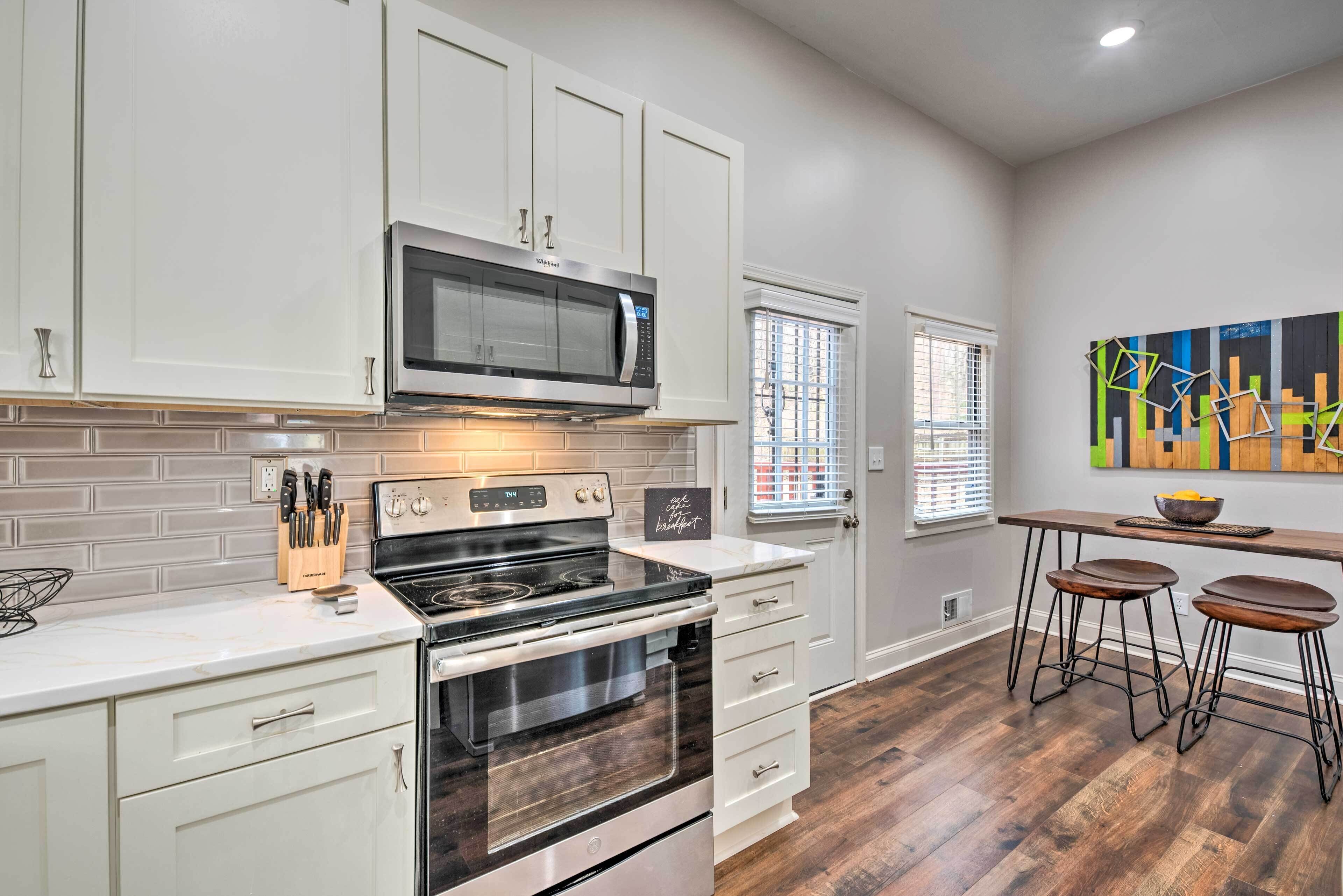 A kitchen with white cabinets, a stainless steel microwave, a black stove, and a wooden countertop. There are two bar stools and a window with blinds.