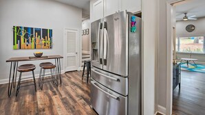 A modern kitchen with a stainless steel refrigerator, wooden stools, and a colorful abstract painting on the wall. - Atlanta Retreat w/ Deck in Greenbriar Area! (Atlanta)