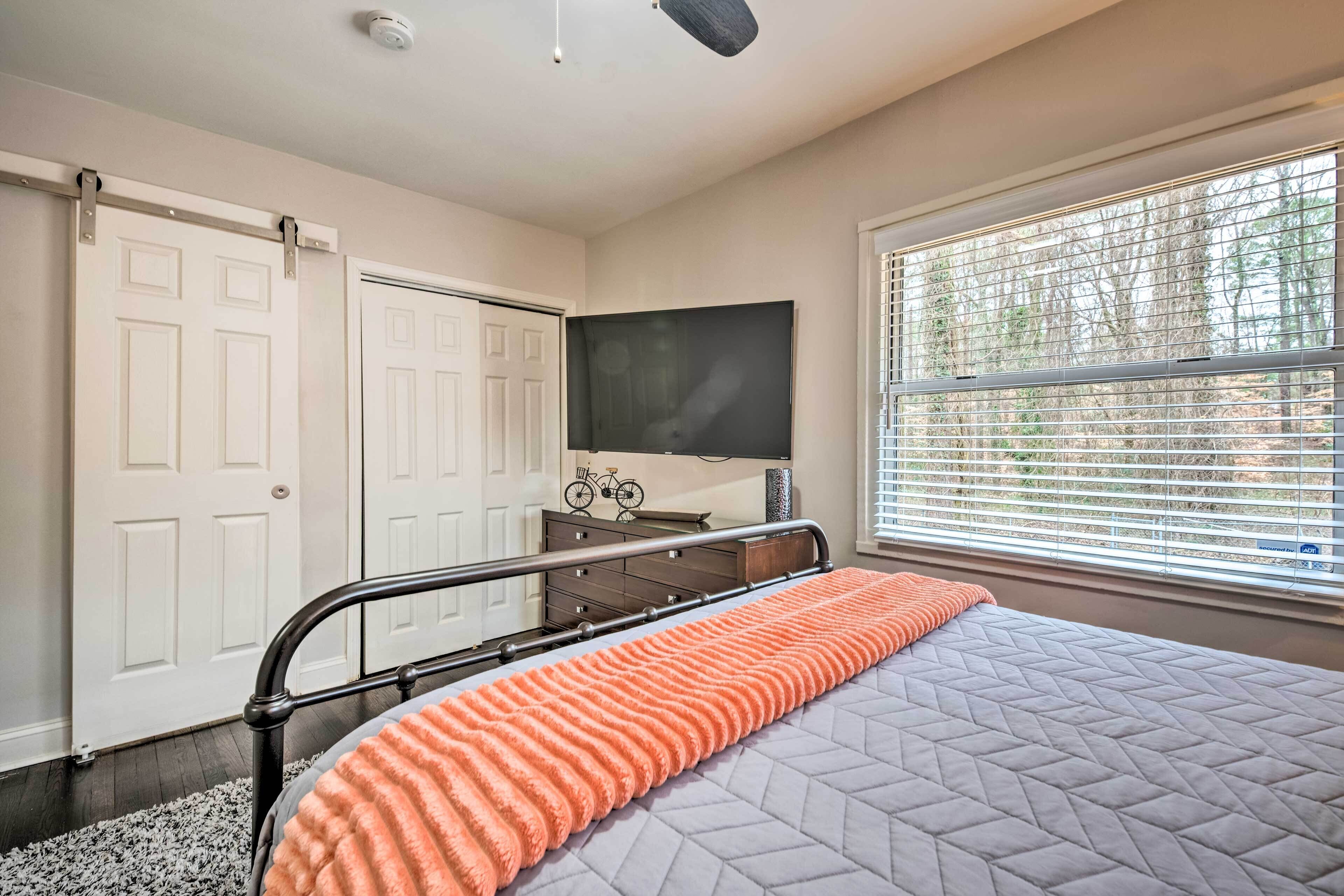 A bedroom with a bed, a dresser, a television, and a window with blinds.