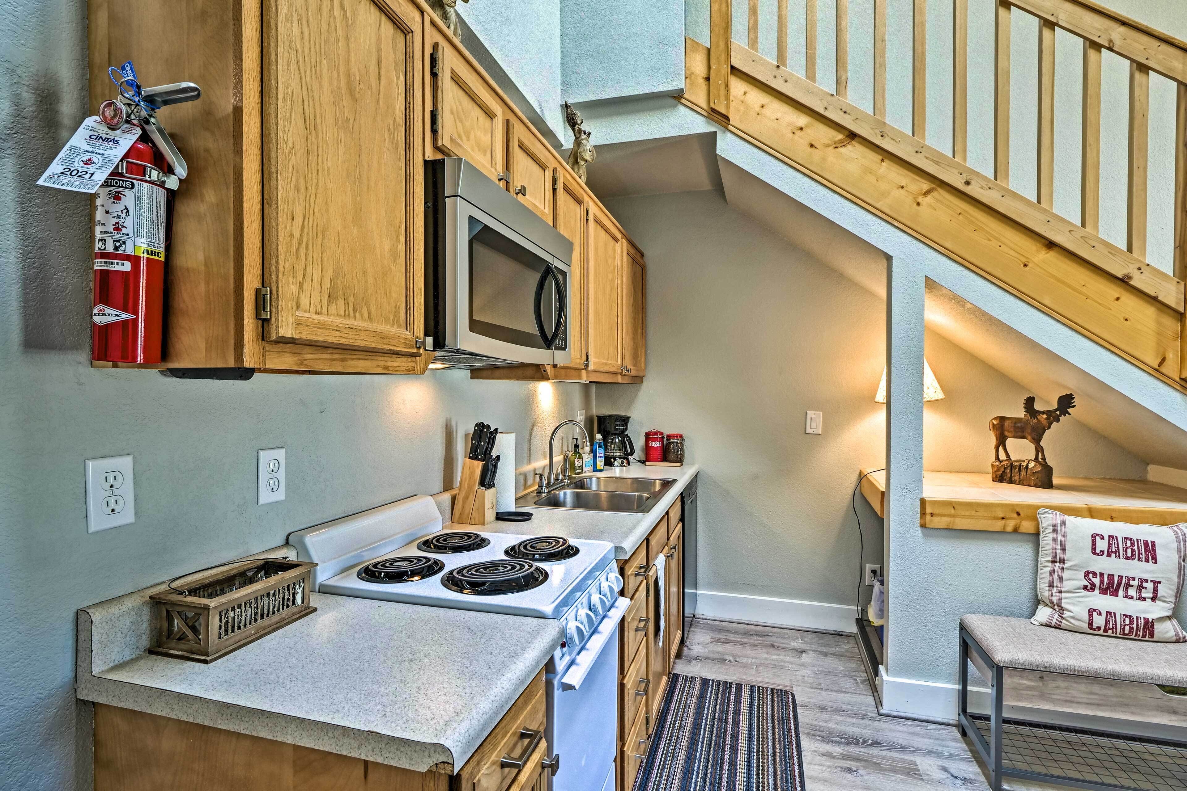 A kitchen with wooden cabinets, a microwave, a stove, and a coffee maker. There is a fire extinguisher mounted on the wall.