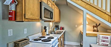 A kitchen with wooden cabinets, a microwave, a stove, and a coffee maker. There is a fire extinguisher mounted on the wall.