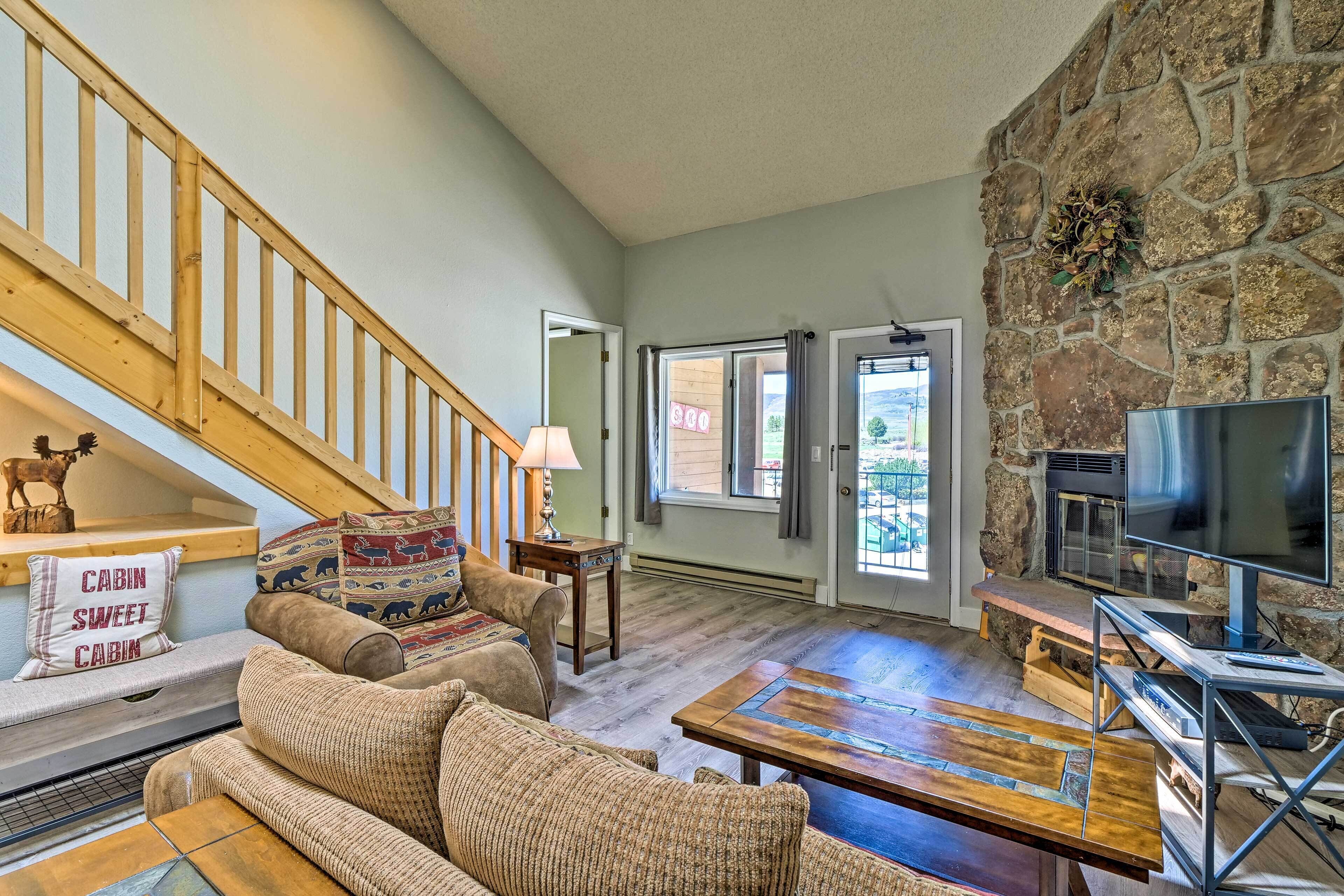 A cozy living room with a stone fireplace, a wooden staircase, and a comfortable seating area.