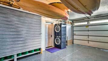 A garage with two surfboards mounted on the ceiling, a washing machine, and a door leading to a garage.