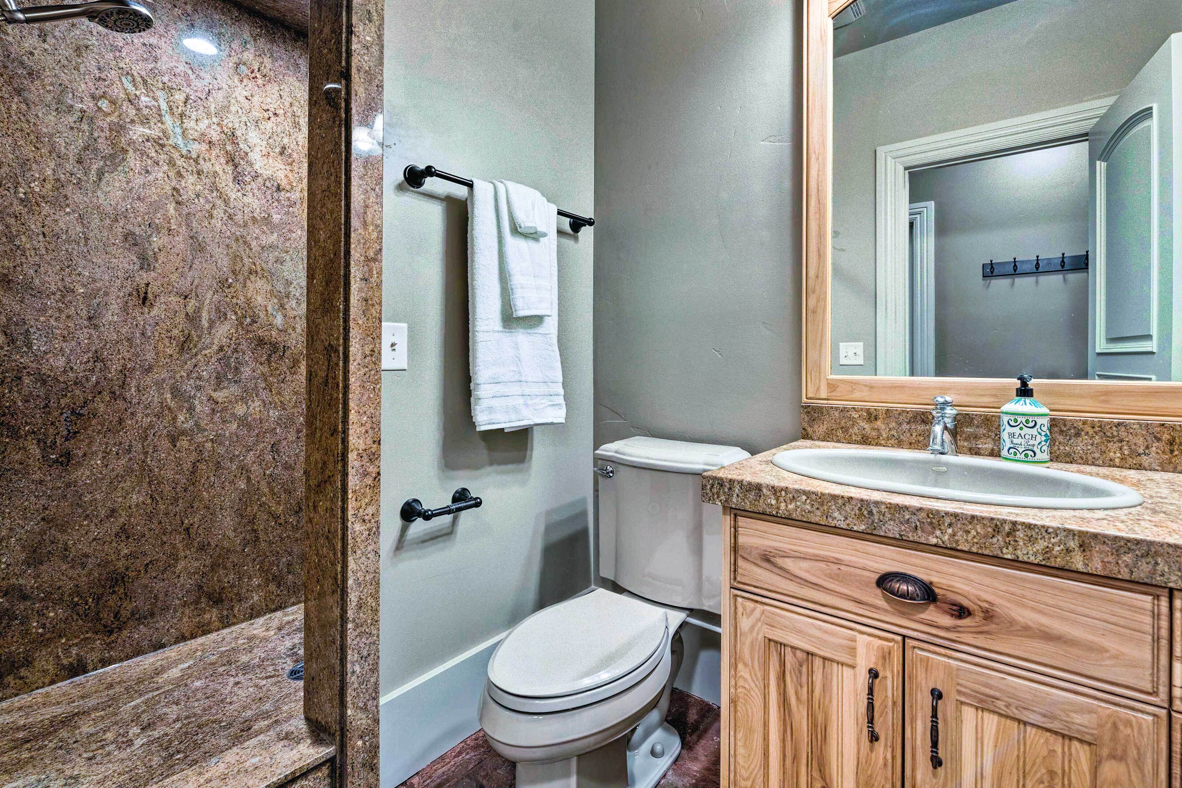A bathroom with a marble shower, a toilet, a sink with a wooden vanity, and a mirror.