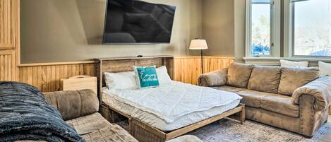 A cozy room with a bed, two sofas, a flat-screen TV, and a window with a view.