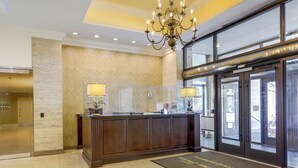 A reception area with a marble wall, a wooden reception desk, two lamps, and a glass door leading outside. - Colorful Atlanta Vacation Rental - Walk to Dtwn! (Atlanta)