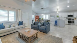 A spacious living room with a sofa, two armchairs, a coffee table, and a ceiling fan. A kitchen with white cabinets and appliances is visible in the background. - Private Pool & Furnished Deck: Port Aransas Home! (Port Aransas)