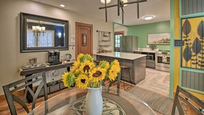 A modern kitchen with a dining area, featuring a large island, a coffee station, and a vase with sunflowers. - 2 Mi to Central Ave: Quaint Hot Springs Home! (Hot Springs)