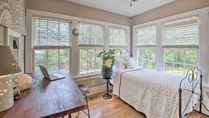 A bedroom with a bed, a desk with a laptop, a lamp, and a window with a view of trees. - 2 Mi to Central Ave: Quaint Hot Springs Home! (Hot Springs)