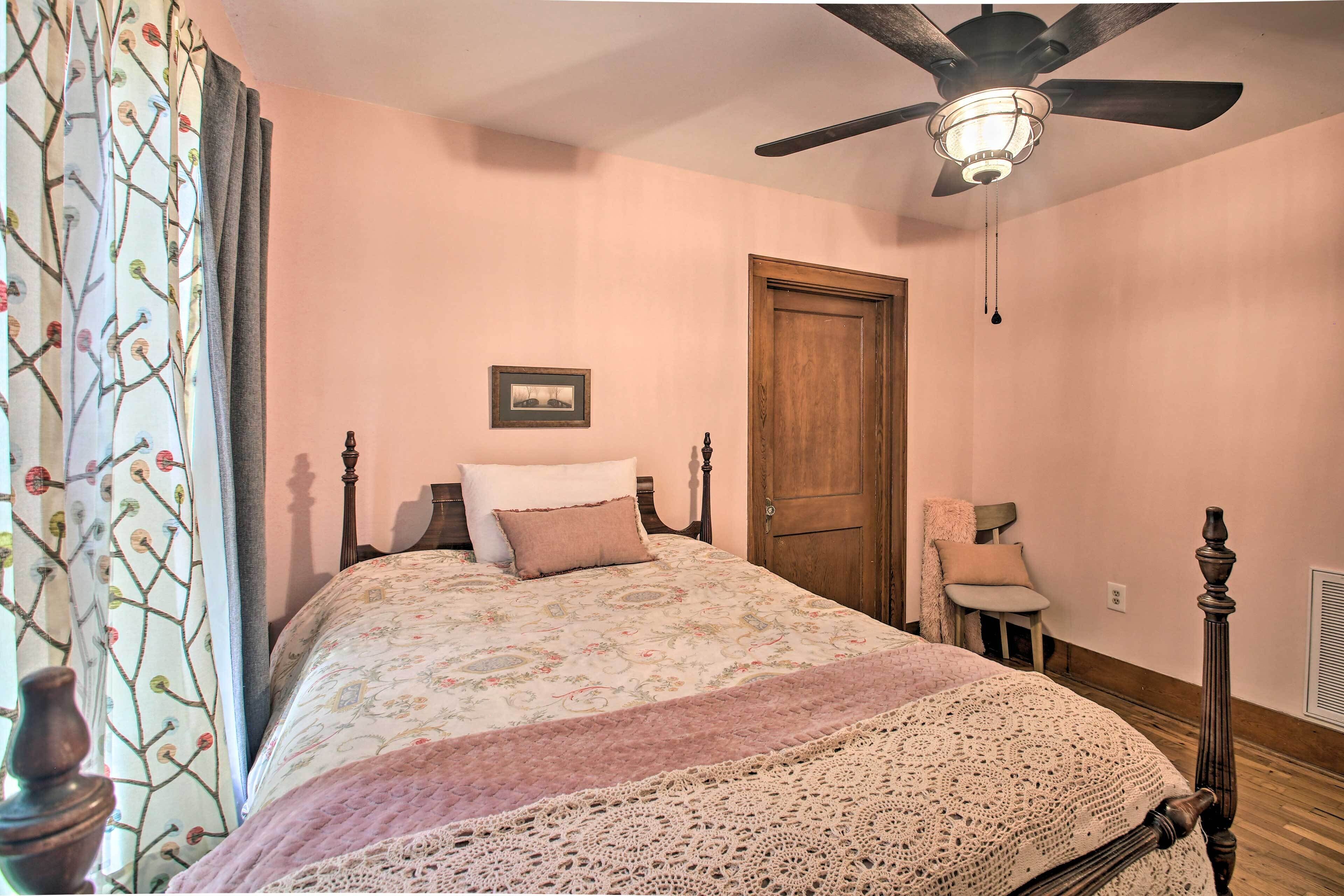 Ein Schlafzimmer mit einem Bett, einer Holztür, einem Deckenventilator und einem kleinen Tisch mit Stuhl.