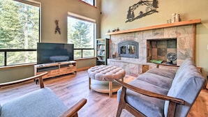 Una sala de estar acogedora con chimenea, televisor y grandes ventanales con vistas a árboles.