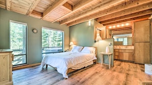 Un dormitorio con techo de madera, una cama, una mesita de noche, una lámpara, una ventana y vistas al exterior.