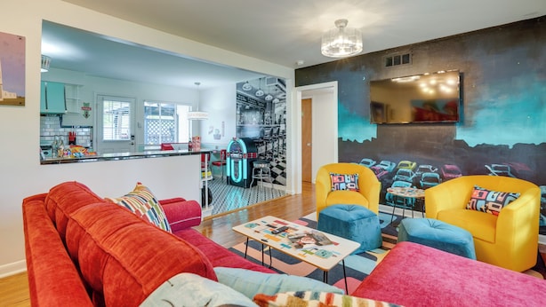 A living room with a red sofa, yellow armchairs, and a coffee table. There is a kitchen in the background with a jukebox. - San Antonio Retreat w/ Private Hot Tub & Gas Grill (San Antonio)