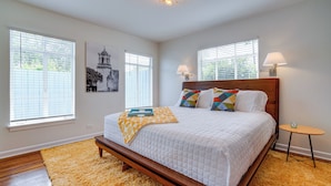 A bedroom with a wooden bed, white bedding, a yellow rug, and two windows with blinds. - San Antonio Retreat w/ Private Hot Tub & Gas Grill (San Antonio)