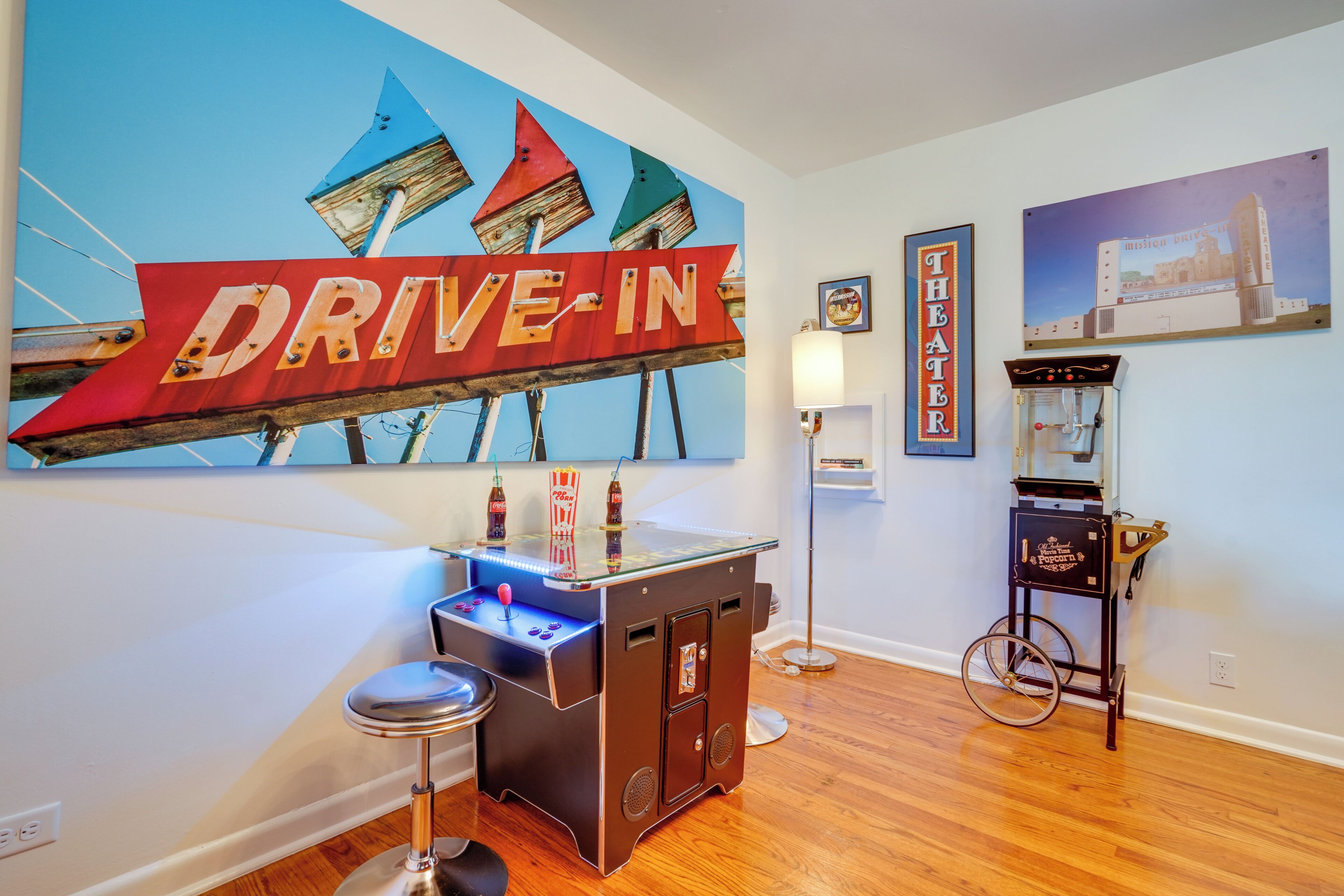 Una habitación con un letrero de cine drive-in, una pequeña zona de bar y una máquina de videojuegos antigua.