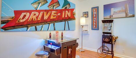 Una habitación con un letrero de cine drive-in, una pequeña zona de bar y una máquina de videojuegos antigua.