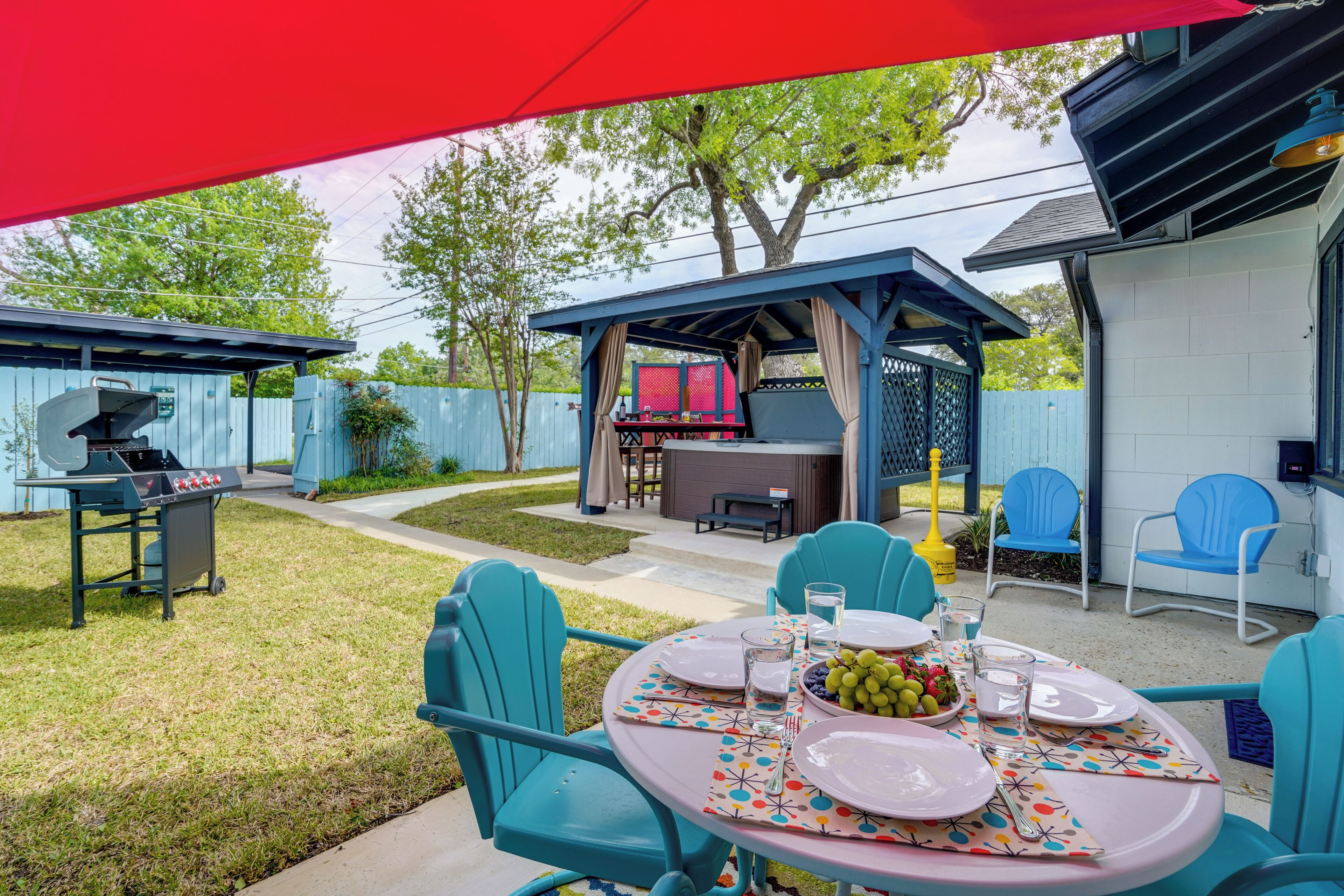 An outdoor patio with a round table set for four, surrounded by turquoise chairs.