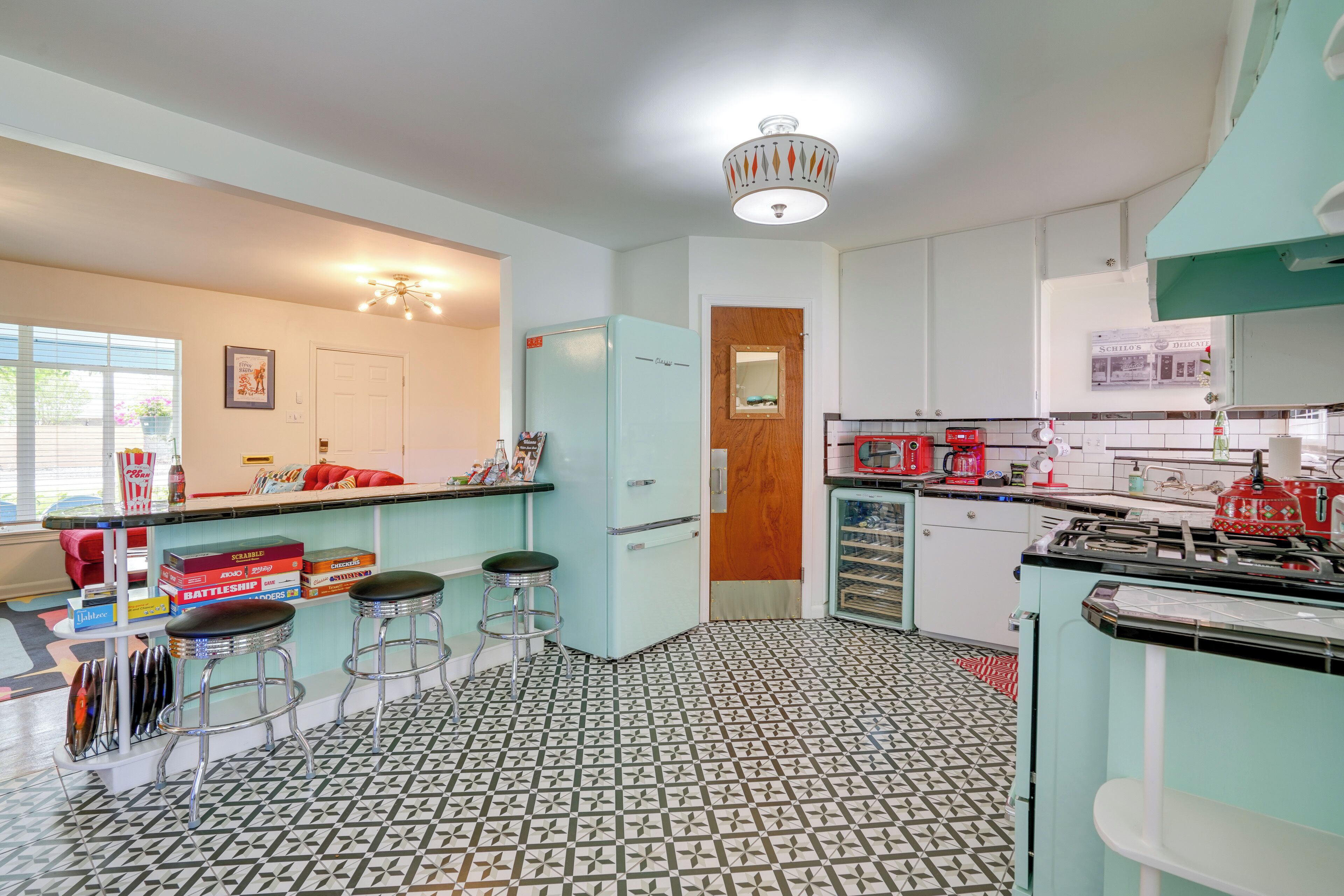 A retro kitchen with a patterned floor, a light blue refrigerator, and a red coffee maker.