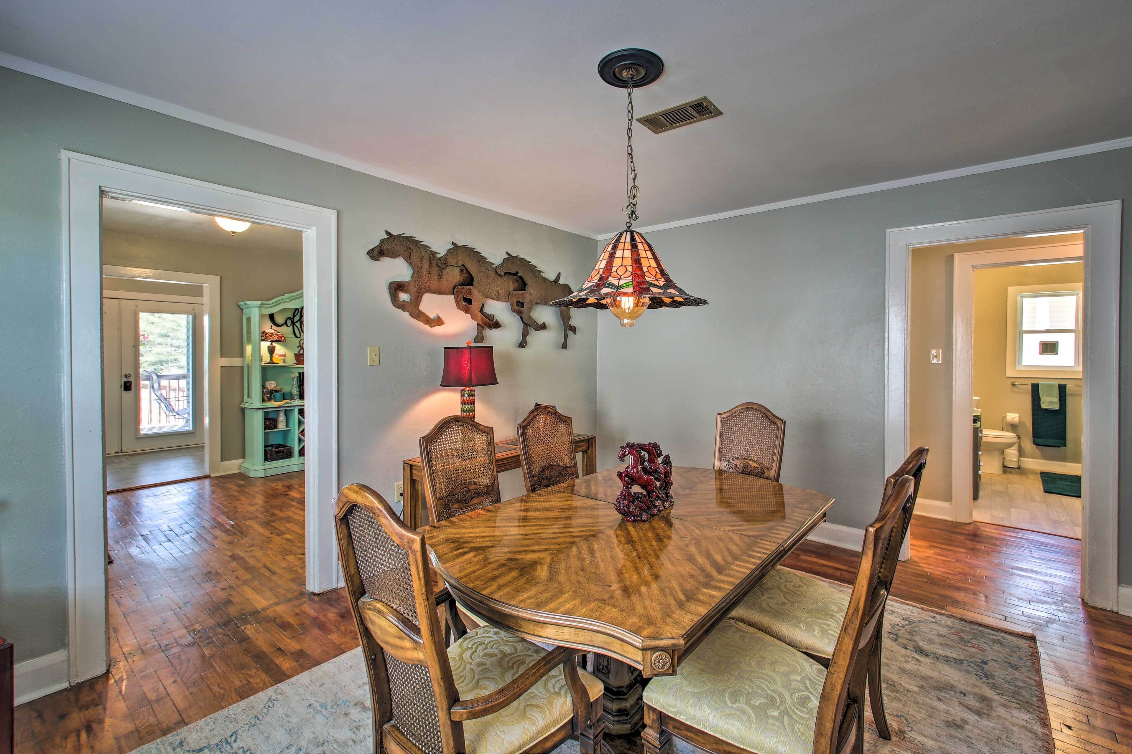 A dining room with a wooden table, six chairs, a chandelier, and a decorative horse sculpture.
