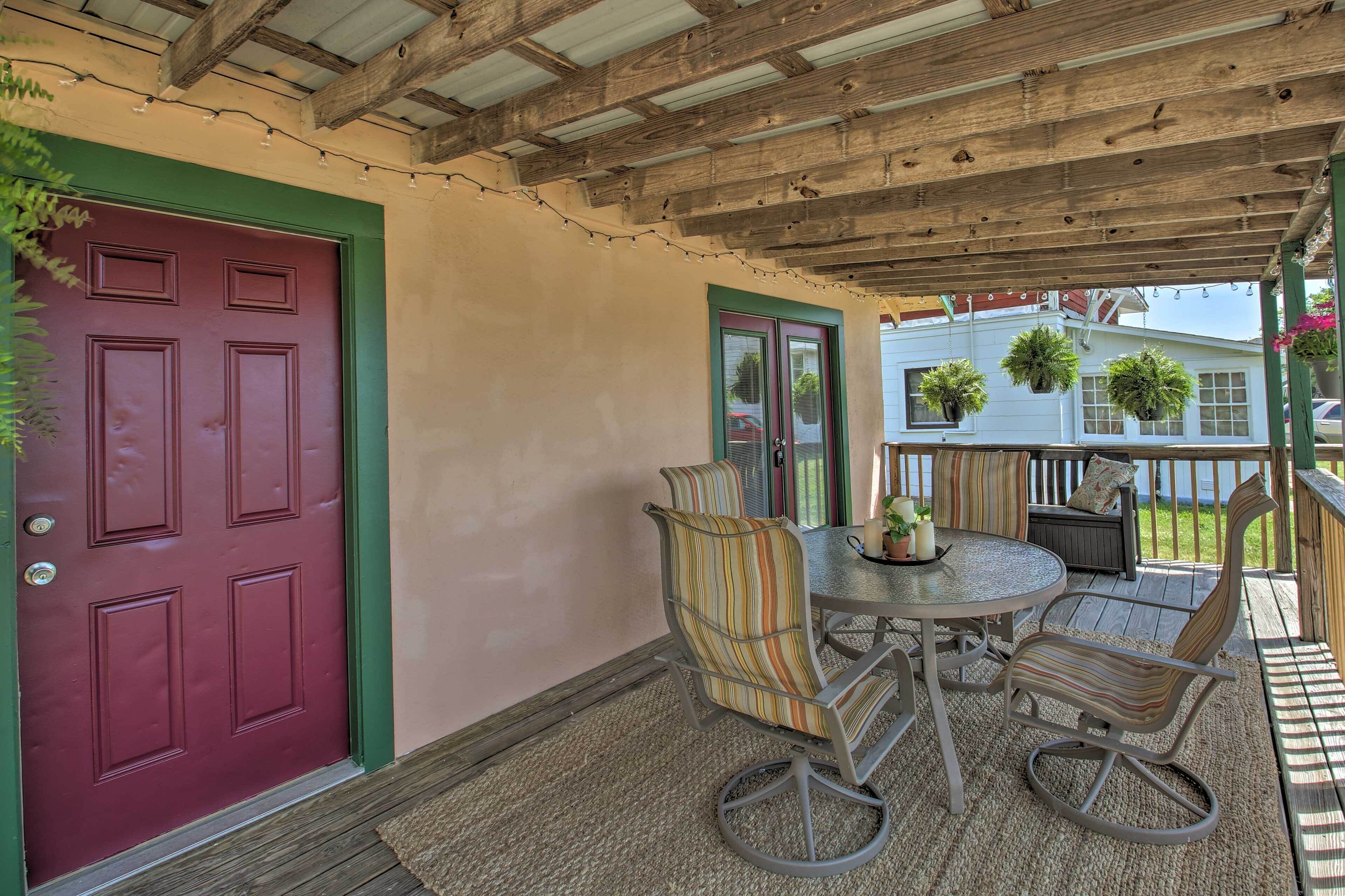 A covered patio with a red door, a round table, and striped chairs.