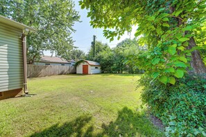 Ein Garten mit Holzzaun, Gartenhaus und Baum mit grünen Blättern.