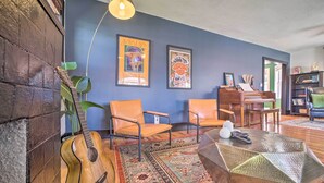 A living room with a guitar, two framed artworks, a coffee table, and a piano. - Amazing Musical Abode in Expo Square Neighborhood! (Tulsa)