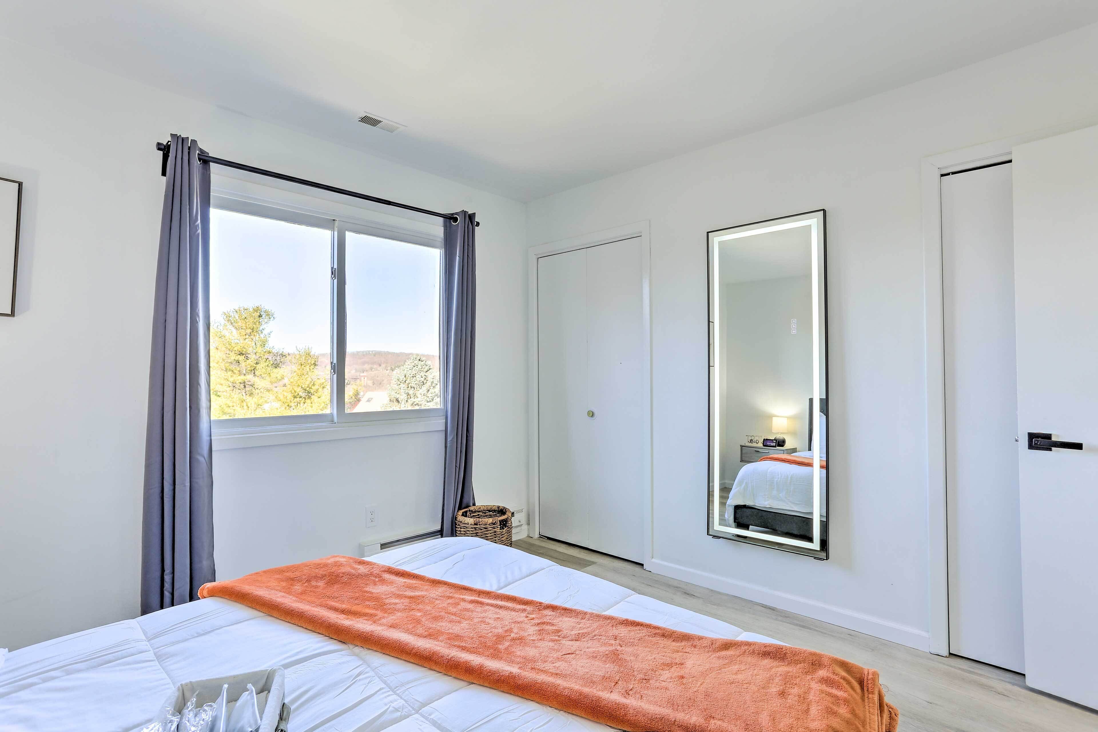 A bedroom with a bed, a large mirror, a window with curtains, and a door.