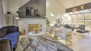 Una sala de estar moderna con chimenea, un sofá, una mesa de centro y un comedor con sillas y un ventilador.