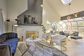 Uma sala de estar moderna com lareira, um sofá, uma mesa de centro e um espaço de jantar com cadeiras e um ventilador.