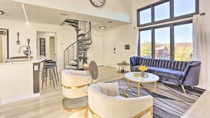 Un salón espacioso con cocina moderna, un ventanal con vistas, un sofá elegante y una original escalera de caracol.