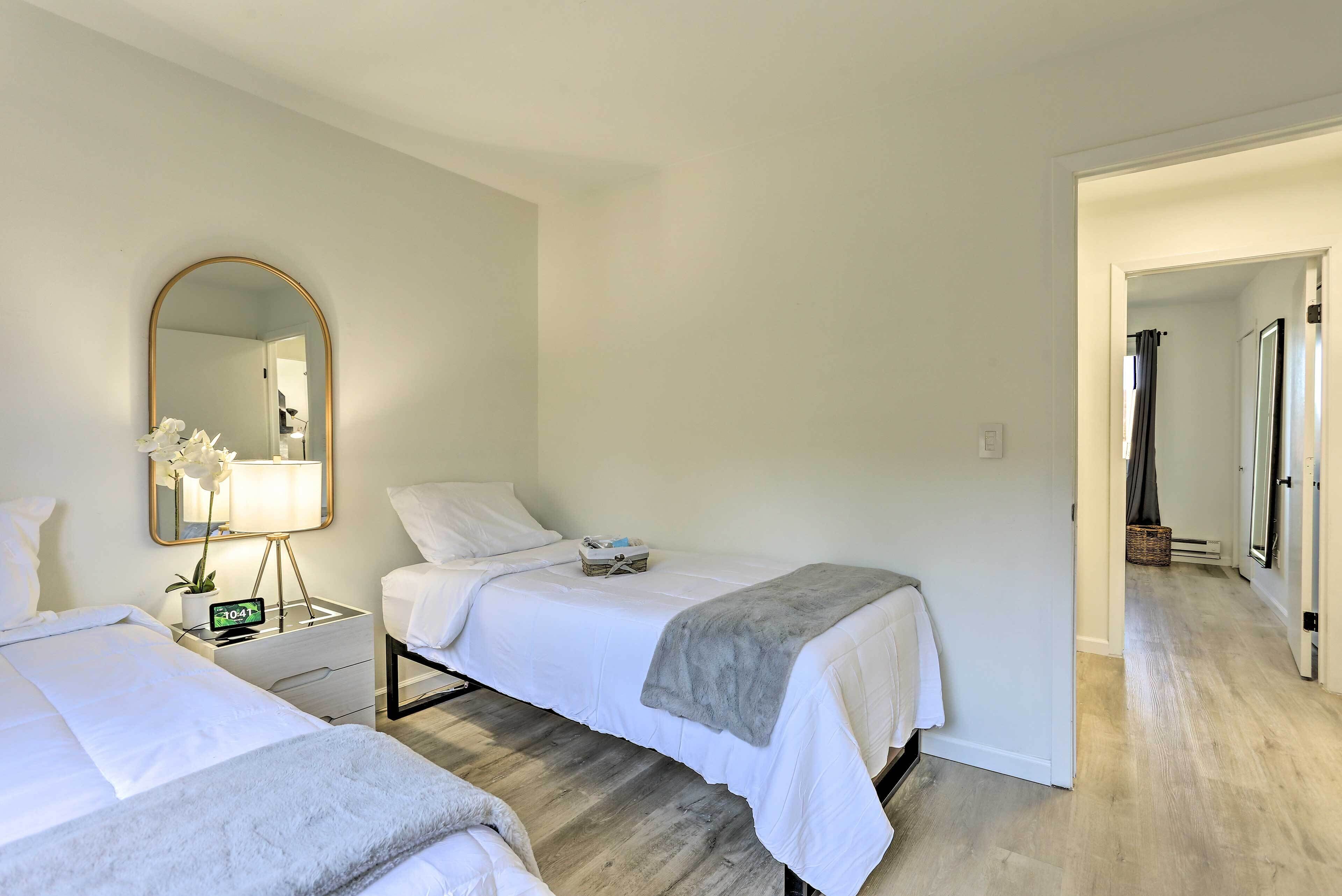 A hotel room with two beds, a bedside table with a lamp, a mirror, and a small plant.