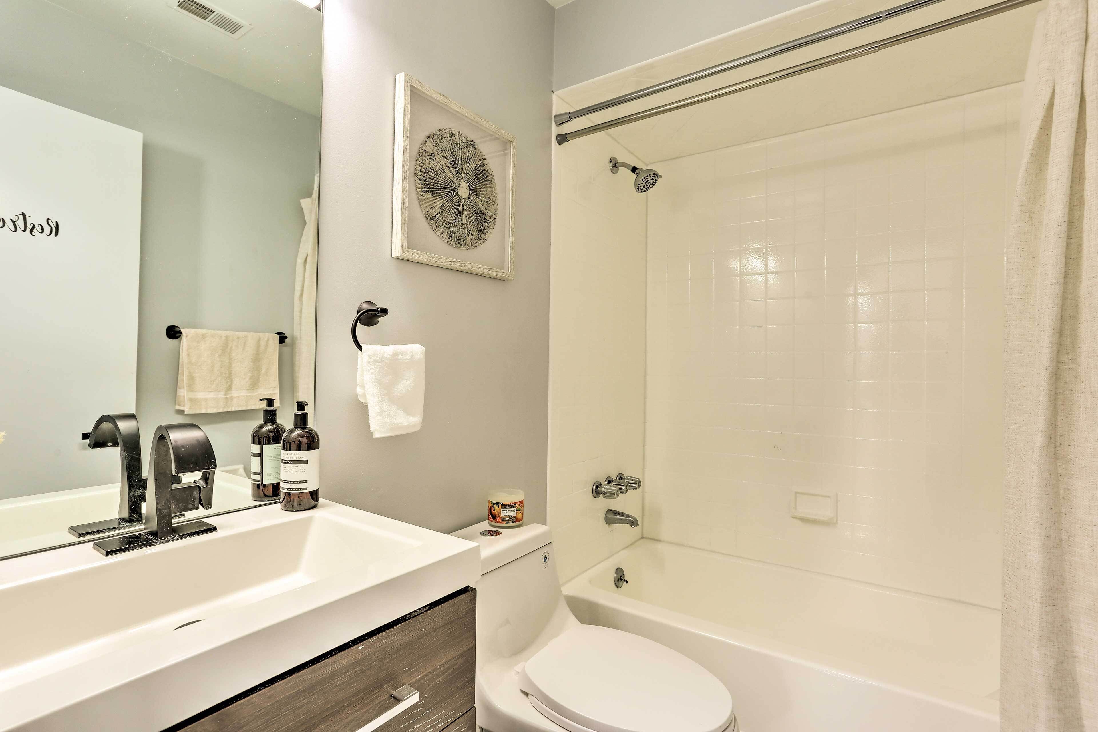 A bathroom with a white sink, a mirror, a towel, a shower, and a toilet.