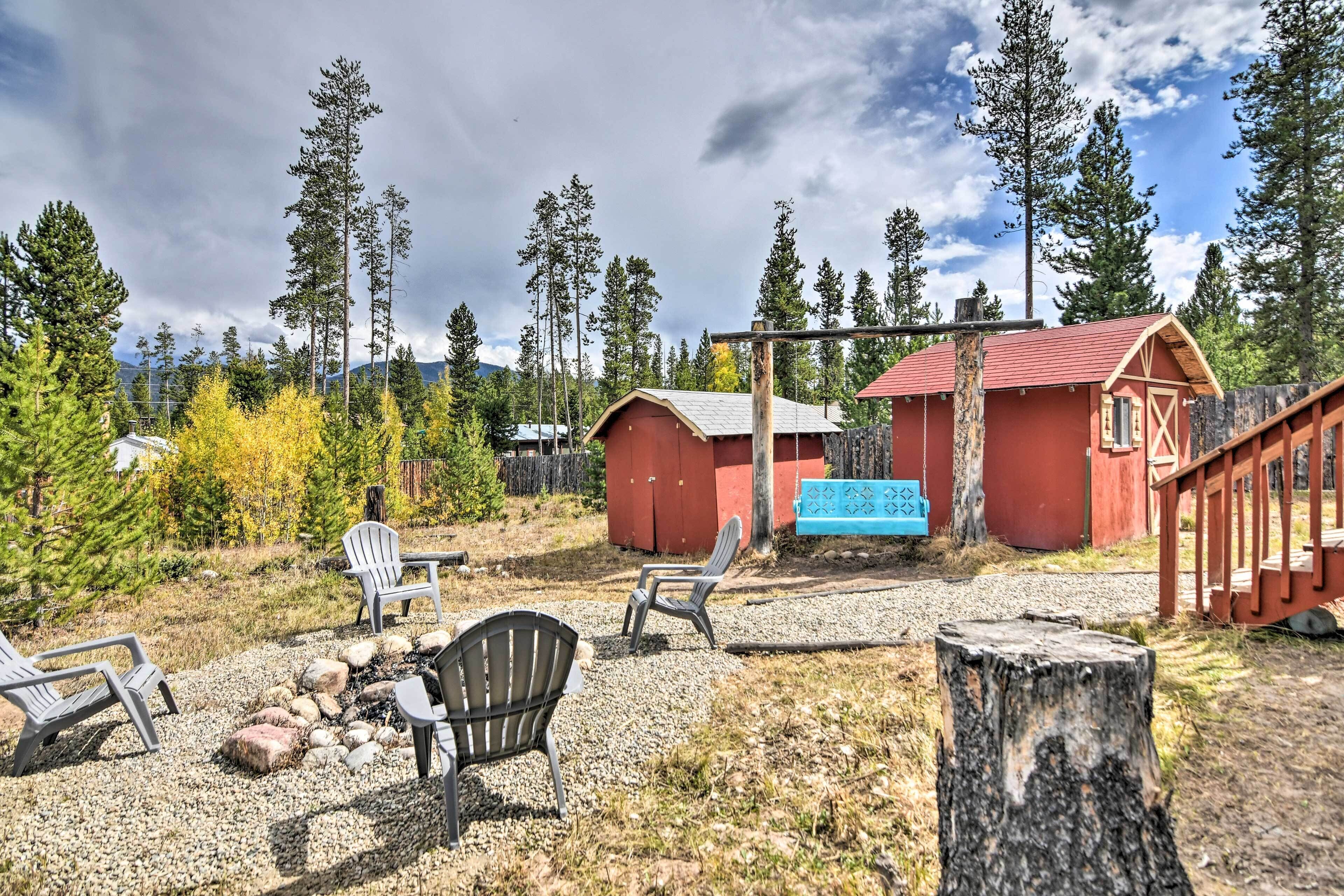 A rustic cabin with a red exterior, surrounded by a gravel area with outdoor seating and a fire pit.