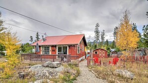 A red cabin with a metal roof, a porch, and a small shed in a forested area.