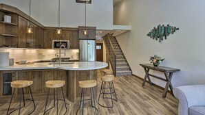 Une cuisine moderne avec des meubles en bois, un îlot central doté de tabourets, un escalier et un élément décoratif mural.
