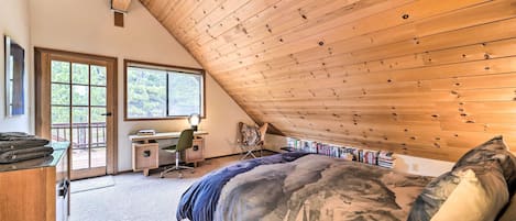 A bedroom with a sloped ceiling, a bed with camouflage bedding, a desk with a chair, and a bookshelf.