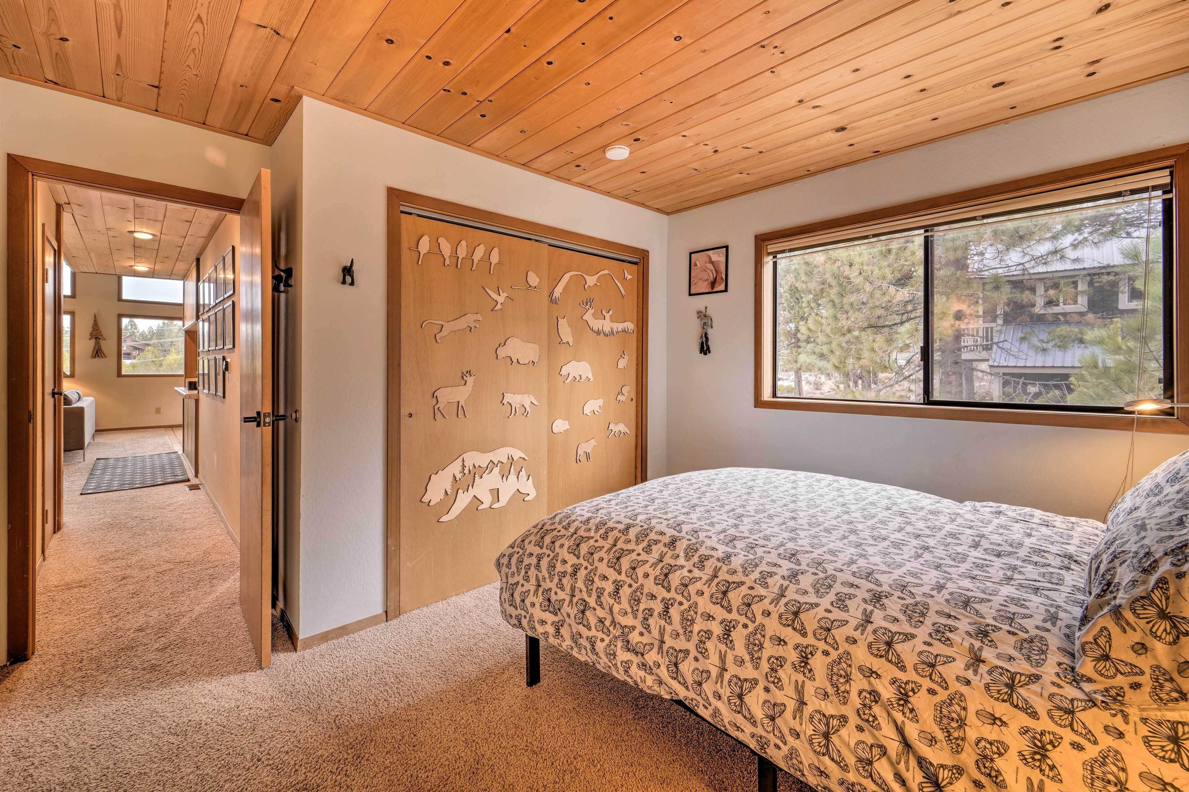 A bedroom with a wooden ceiling, a large window, a bed with a patterned blanket, and a door with animal cutouts.