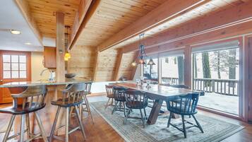 A spacious kitchen with a wooden table and chairs, large windows, and a view of the snowy outdoors.