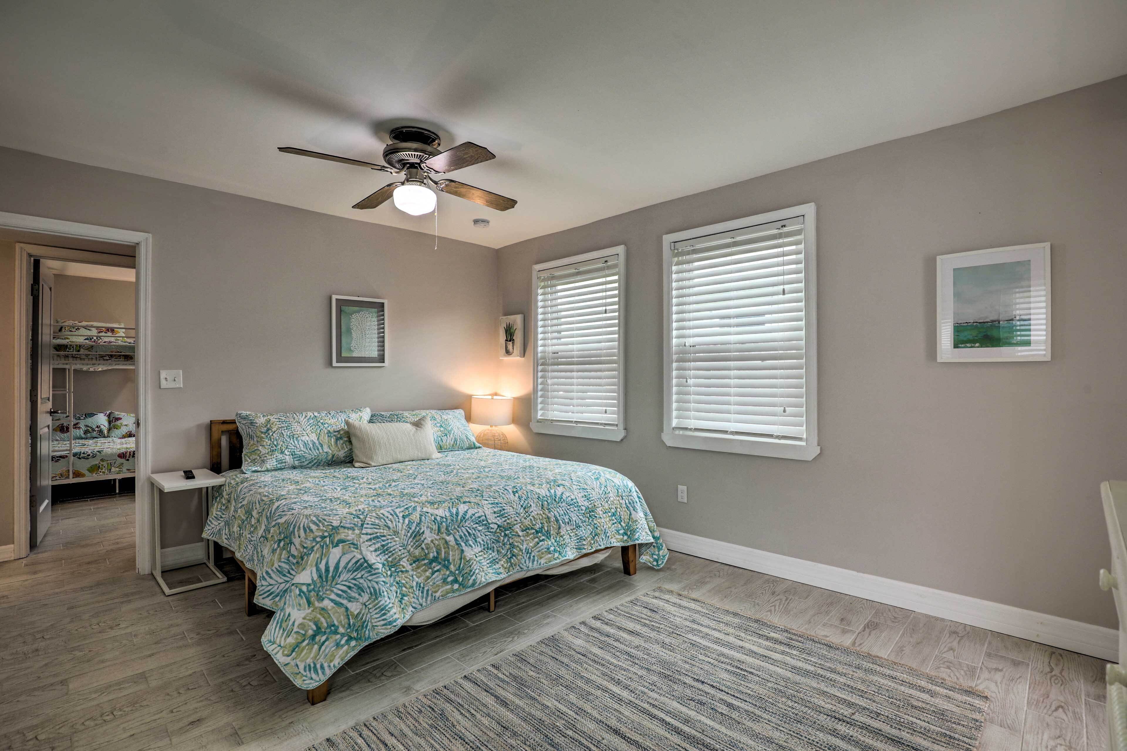 A bedroom with a bed, a ceiling fan, a nightstand, a lamp, and a window with blinds.