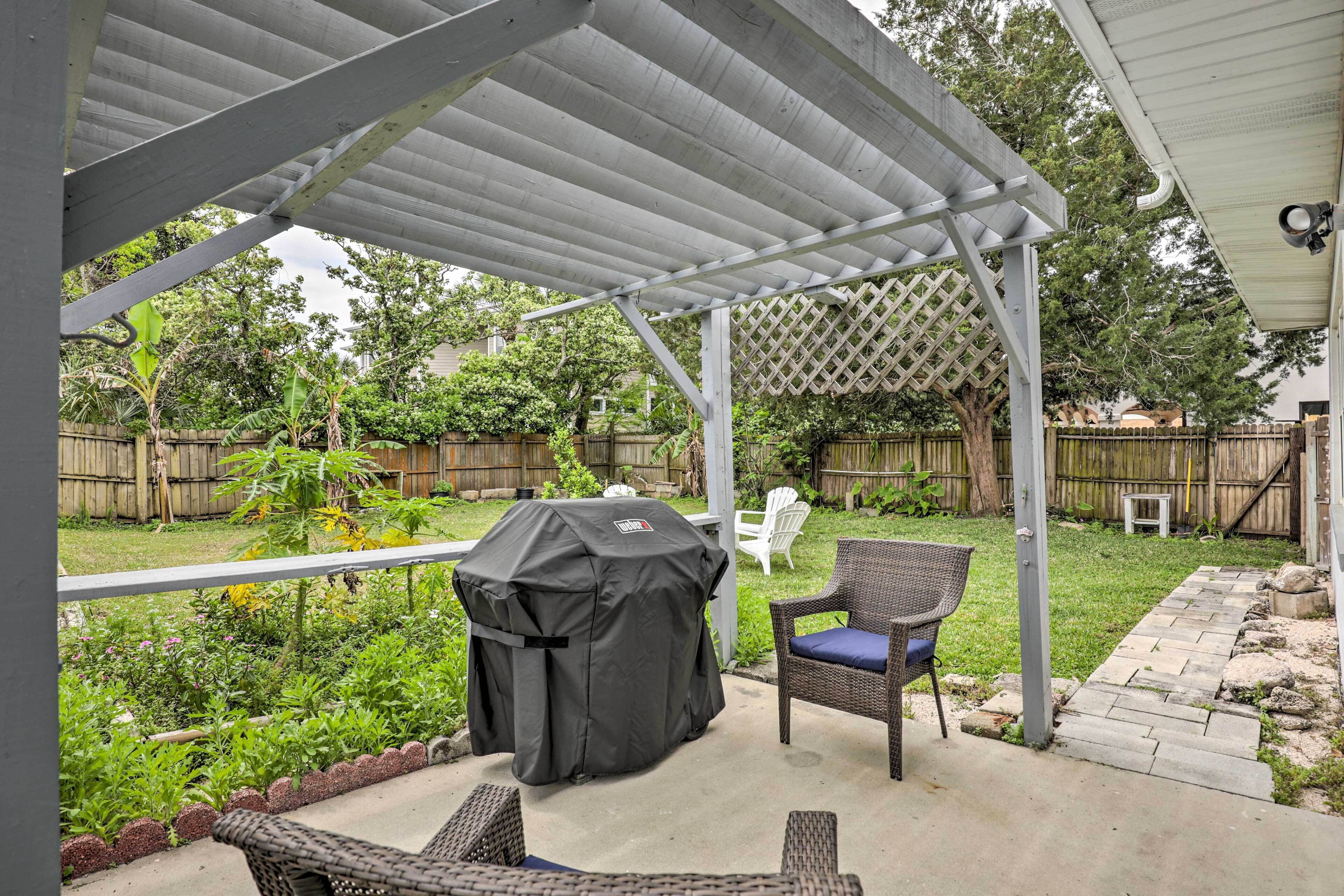 A covered patio area with a grill, outdoor furniture, and a garden view.