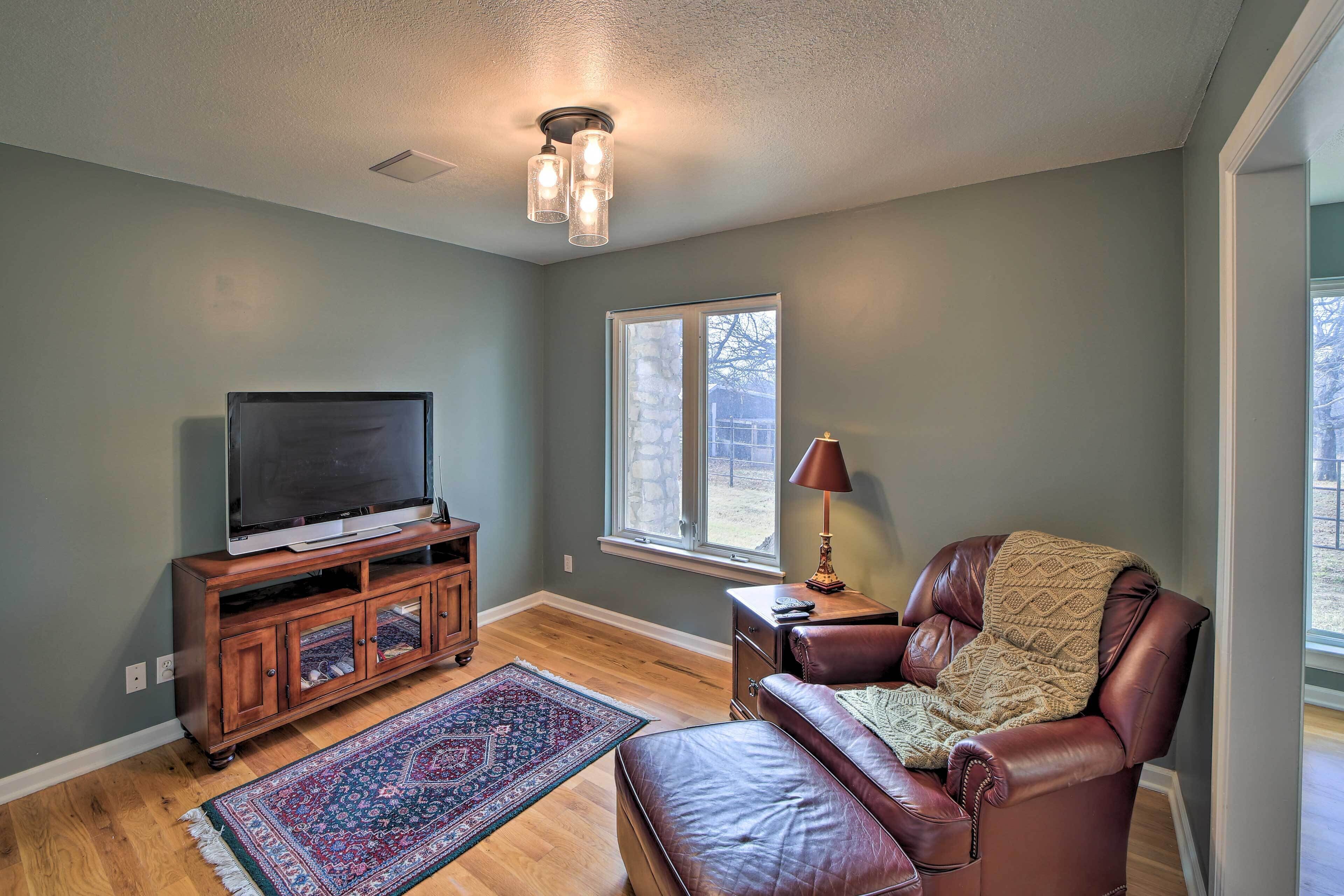 A living room with a television on a wooden cabinet, a leather chair, a rug, and a window with a view of the outside.