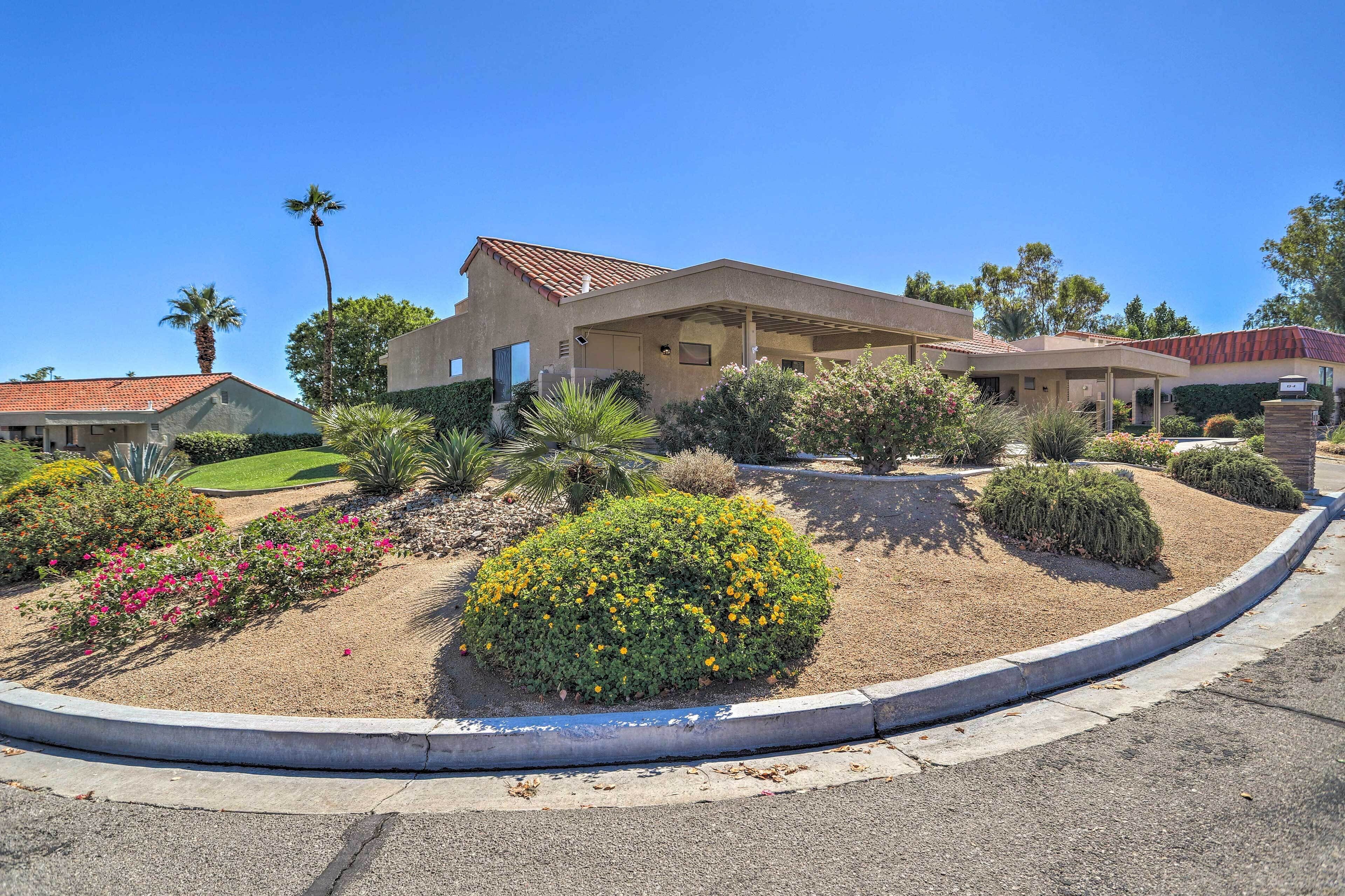 A modern house with a covered patio, surrounded by landscaped gardens and palm trees.