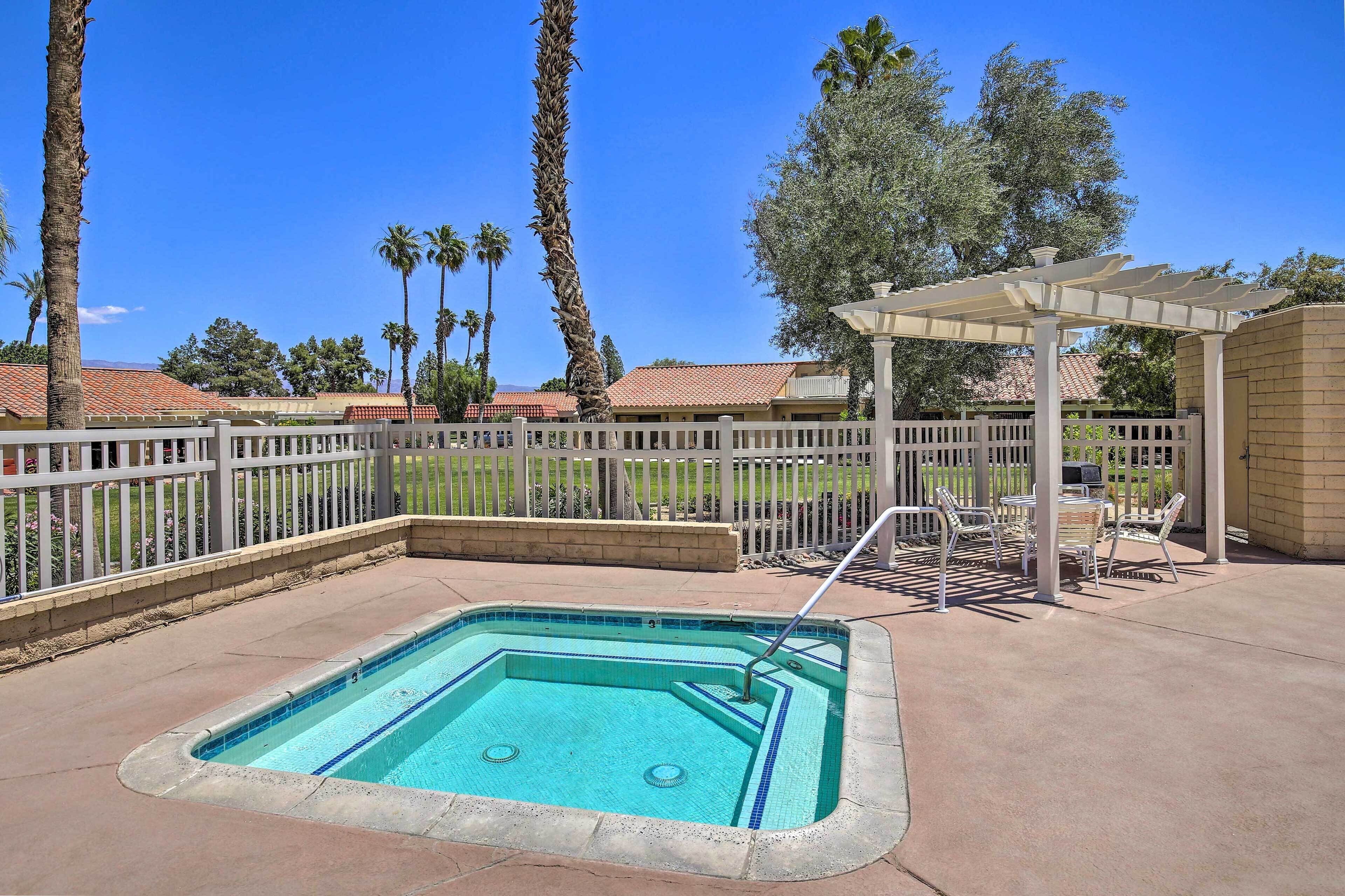 A swimming pool with a white pergola and lounge chairs, surrounded by a fence and palm trees.