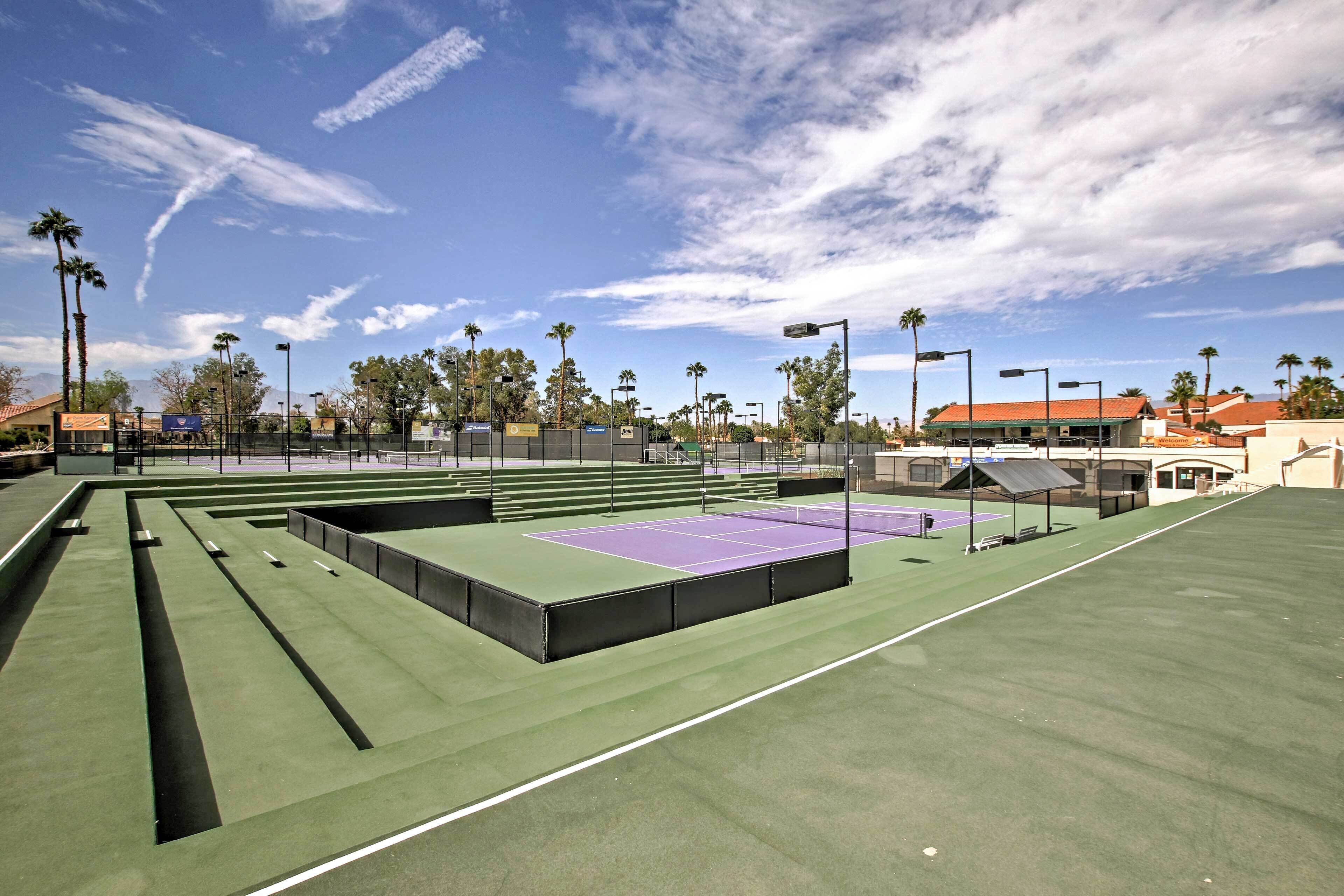 Ein Tennisplatz mit Sitzbereichen und einer überdachten Zuschauertribüne.