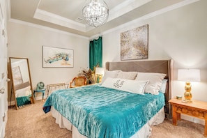 A bedroom with a large bed, a bedside table with a lamp, a mirror, and artwork on the walls. - Gorgeous College Station Townhome w/ Patio! (College Station)