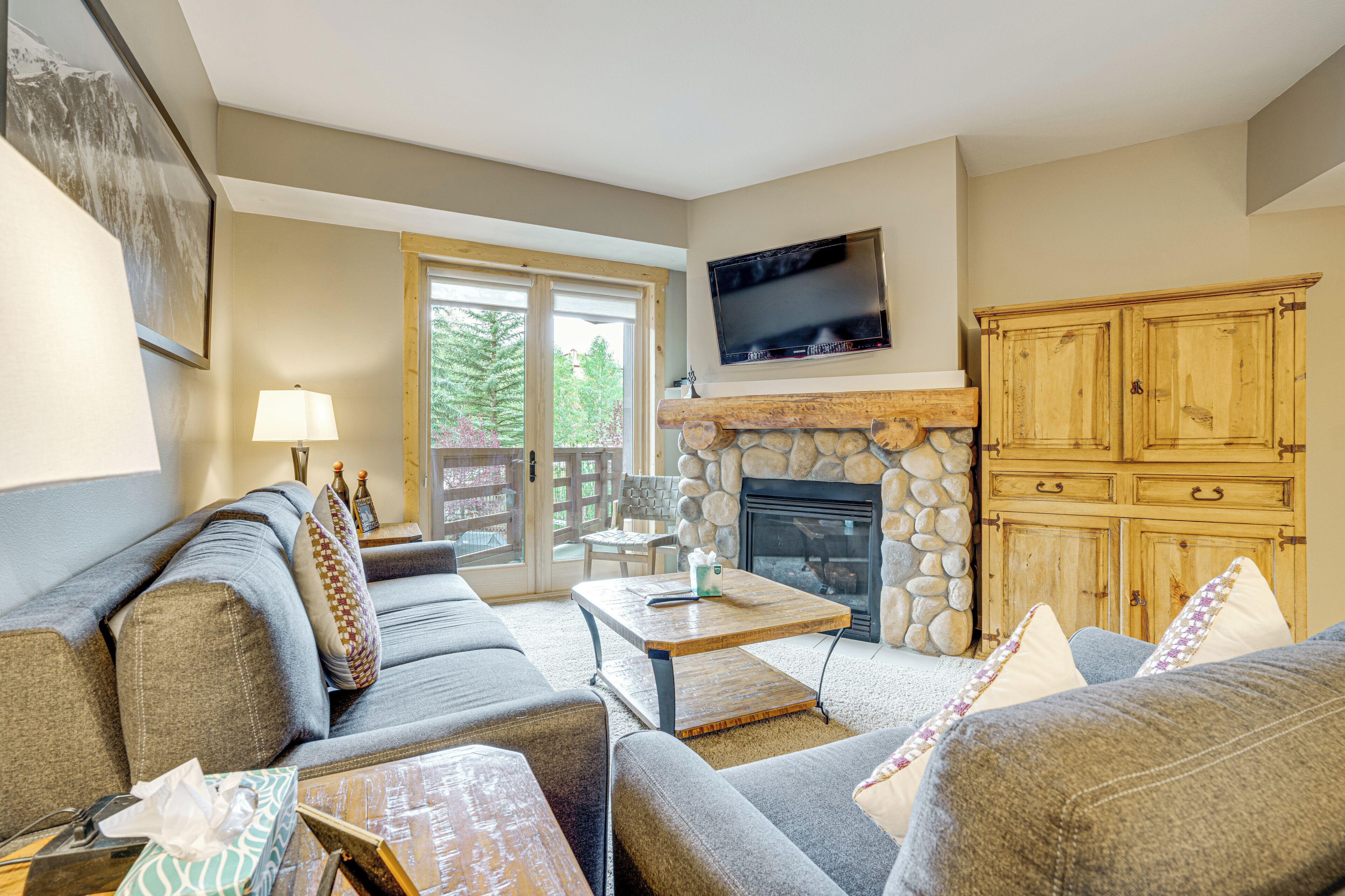 A living room with a stone fireplace, a television mounted above it, and a large wooden cabinet.