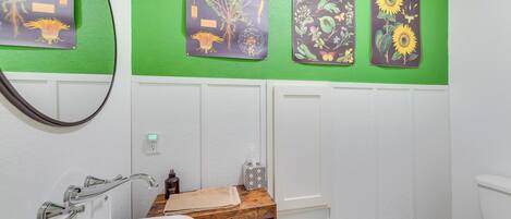 Un baño con pared verde, bañera blanca, tocador de madera y un inodoro.