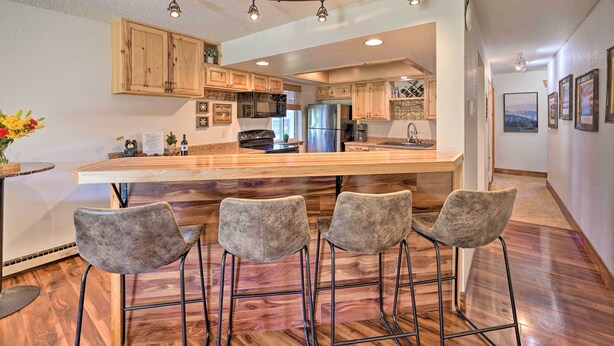 A modern kitchen with wooden cabinets, a large island with bar stools, and stainless steel appliances. - Cozy & Chic Mountain Condo w/ Community Perks (Fraser)