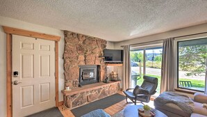 A cozy living room with a stone fireplace, comfortable seating, and a large window offering a view of the outdoors. - Cozy & Chic Mountain Condo w/ Community Perks (Fraser)